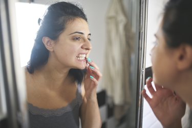 a woman looking at her mouth in the mirror because she has itchy gums
