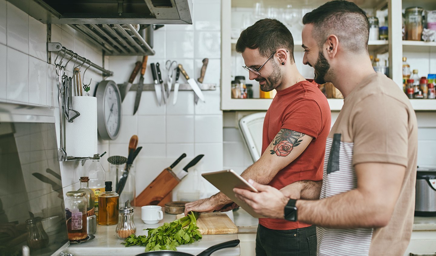 Two men cooking in the kitchen using an ipad to refer to a recipe