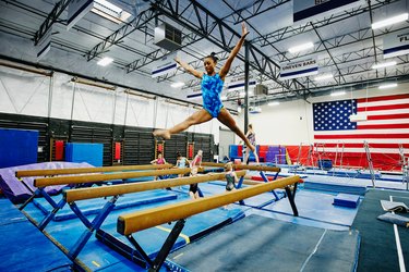 gymnast practicing balance beam wearing blue leotard in front of american flag