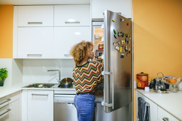 a person with blonde curly hair wearing a colorful sweater and looking in the fridge because they have early pregnancy hunger