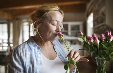 Older adult with a blonde messy bun smelling a pink flower, to represent the loss of smell due to aging