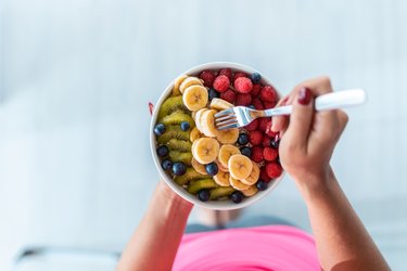 overhead view of a person with red fingernails holding a bowl with fresh fruit