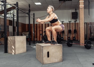 Sporty woman doing box jumps in gym. Sportwoman jumping on wooden box on health gym club.