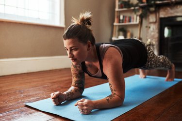 Woman doing a forearm plank during an at-home workout on a blue yoga mat