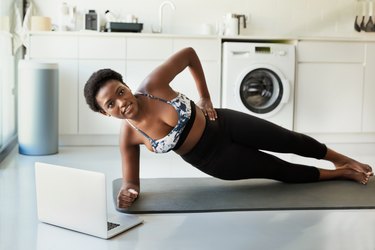 Woman doing a side plank during an ab workout at home with her laptop