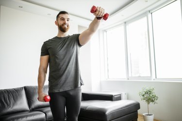 fit man doing a light dumbbell arm workout in his living room with a pair of red dumbbells