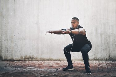 Man trying to do a squat against a concrete wall