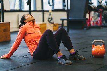 a person sitting down in a gym exhausted from a workout next to an orange kettlebell