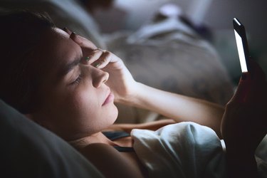 Woman in bed with a headache looking at smartphone