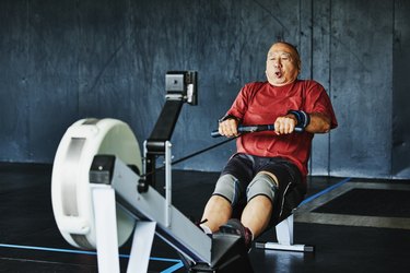 Older adult wearing a red T-shirt and black shorts doing a workout on a rowing machine.