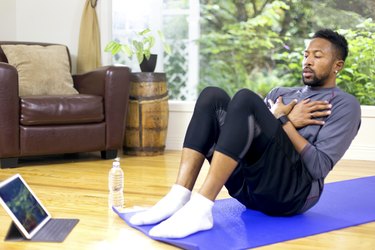 black man sit ups in living room on a blue yoga mat with tablet