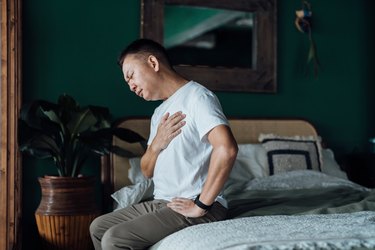 man sitting in bed with his hand over his heart because he woke up with chest pain
