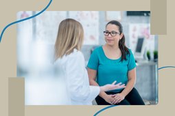 woman in teal t-shirt and glasses speaking with female doctor about PCOS