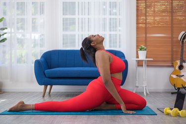 Person in red leggings and red sports bra practicing cobra yoga pose for flexibility on a blue yoga mat in a living room with a blue couch