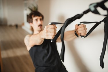 adult man practicing suspension training at modern home