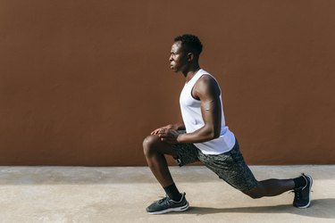 Young man doing stretching exercises against brown wall