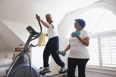 older couple working out on an elliptical machine and lifting dumbbells at home